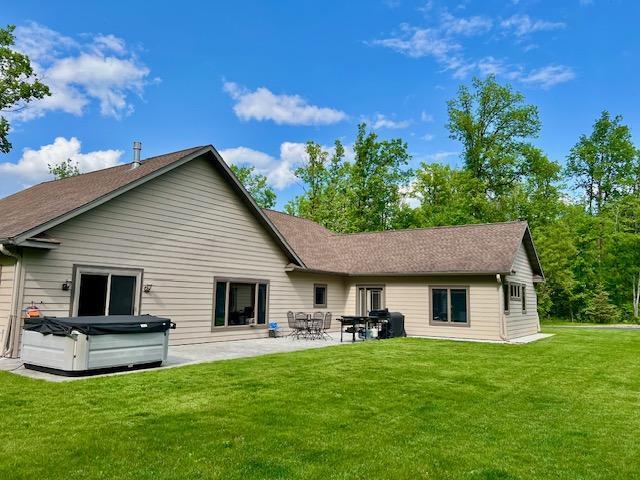 23567 Timber Trail Dr, Bemidji, MN 56601 - rear view of house featuring a hot tub, a patio, a lawn, and roof with shingles