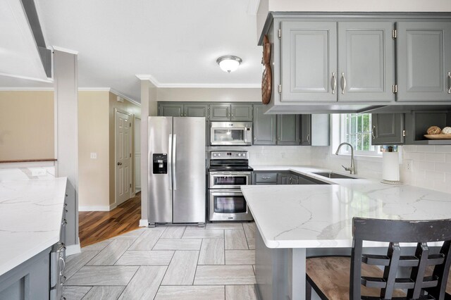 13912 80th St NE, Otsego, MN 55330 - kitchen featuring appliances with stainless steel finishes, a sink, gray cabinetry, a peninsula, and ornamental molding