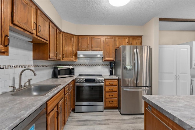 7079 Robinwood Trl, Woodbury, MN 55125 - kitchen featuring appliances with stainless steel finishes, under cabinet range hood, brown cabinets, light wood-style flooring, and a textured ceiling