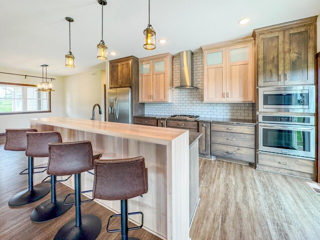 39847 447th St, Sauk Centre Twp, MN 56378 - kitchen featuring appliances with stainless steel finishes, wall chimney range hood, light wood-style flooring, decorative backsplash, and a breakfast bar