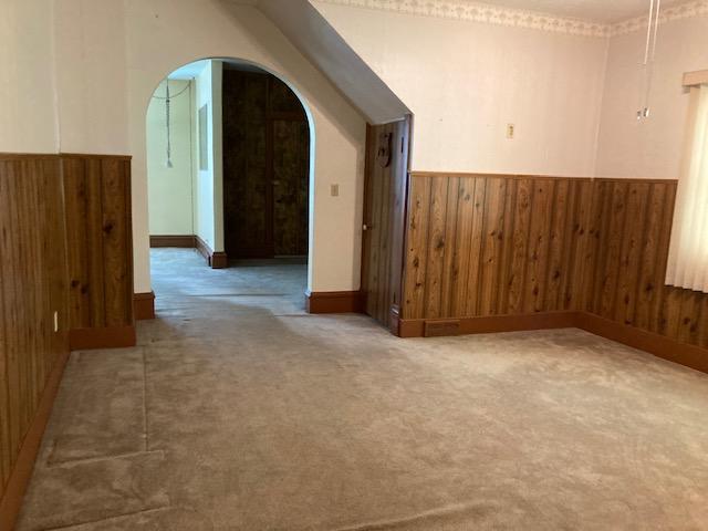 201 Cherry St, Lowry, MN 56349 - spare room featuring arched walkways, wood walls, wainscoting, carpet flooring, and baseboards