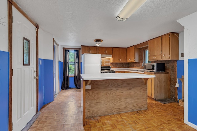 505 Riverside Ave N, Sartell, MN 56377 - kitchen with white appliances, a textured ceiling, under cabinet range hood, brown cabinets, and backsplash