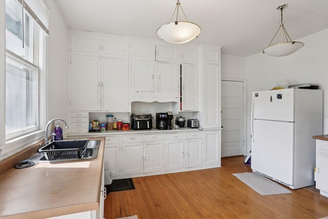 1384 Midway Pkwy, Saint Paul, MN 55108 - kitchen featuring freestanding refrigerator, white cabinets, light wood-type flooring, and hanging light fixtures