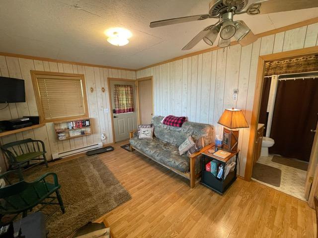 4716 Big Rice Lake Rd NE, Thunder Lake Twp, MN 56672 - living room featuring baseboard heating, a ceiling fan, wood finished floors, ornamental molding, and wooden walls
