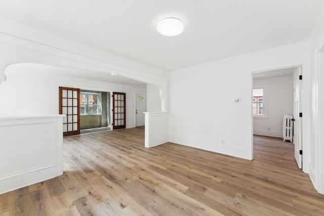 987 Dayton Ave, Saint Paul, MN 55104 - empty room featuring radiator heating unit, healthy amount of natural light, arched walkways, light wood-type flooring, and crown molding