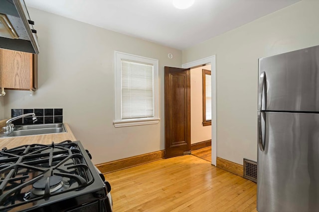 67 Lowry Ave NE, Minneapolis, MN 55418 - kitchen with freestanding refrigerator, black gas stove, and light wood-style flooring