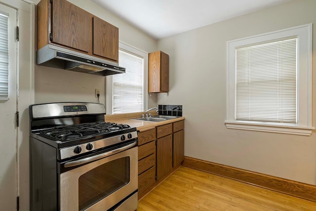 67 Lowry Ave NE, Minneapolis, MN 55418 - kitchen featuring gas range, under cabinet range hood, light wood-type flooring, and brown cabinets