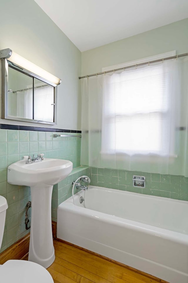 67 Lowry Ave NE, Minneapolis, MN 55418 - bathroom with hardwood / wood-style flooring, a bath, tile walls, and wainscoting