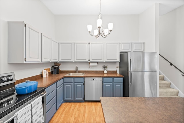 2304 Wildwood Trl, Minnetonka, MN 55305 - kitchen featuring appliances with stainless steel finishes, a chandelier, blue cabinetry, dark countertops, and light wood-style flooring