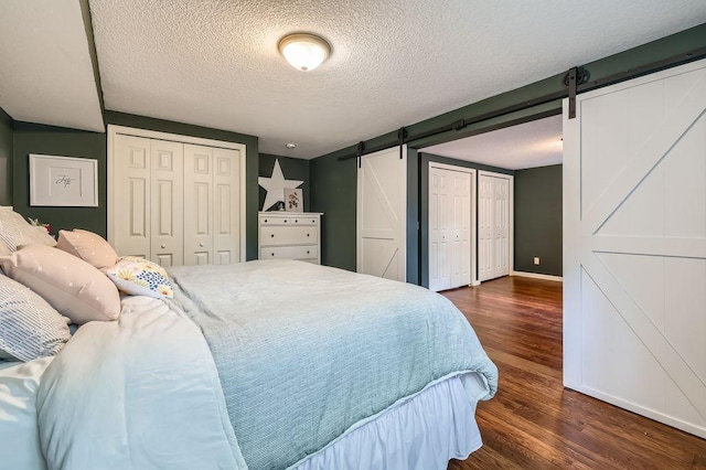 5112 Willow Ln, Minnetonka, MN 55345 - bedroom with a barn door, dark wood finished floors, a textured ceiling, and multiple closets
