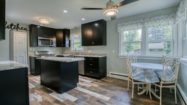 603 15th St SE, Menomonie, WI 54751 - kitchen with a baseboard heating unit, stainless steel appliances, dark cabinets, a kitchen island, and a ceiling fan
