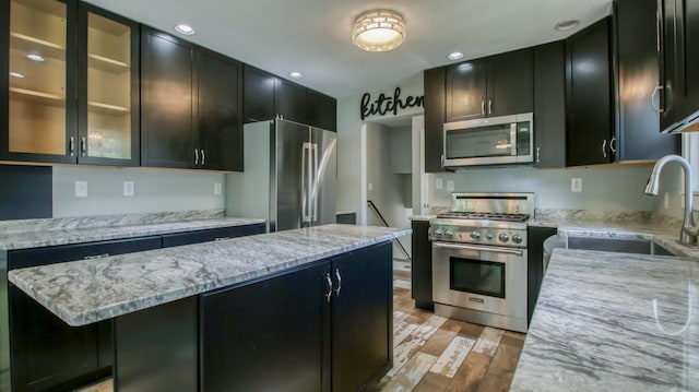 603 15th St SE, Menomonie, WI 54751 - kitchen with appliances with stainless steel finishes, light wood-style floors, a sink, dark cabinets, and glass insert cabinets