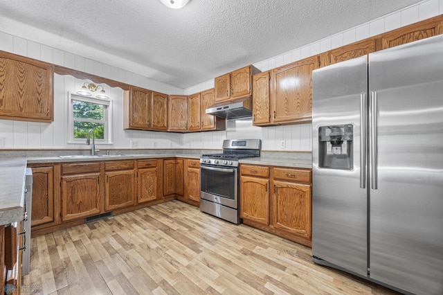 1301 5th Ave N, Moorhead, MN 56560 - kitchen featuring appliances with stainless steel finishes, under cabinet range hood, light wood-style flooring, brown cabinets, and a textured ceiling