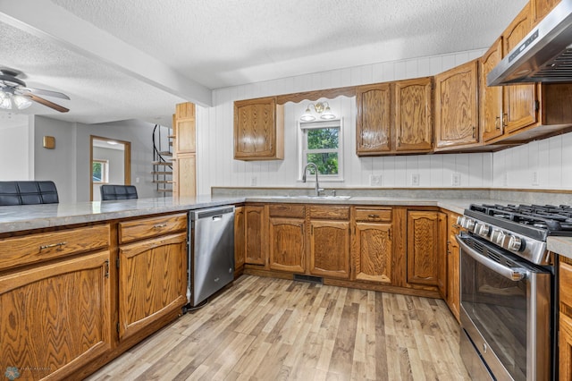 1301 5th Ave N, Moorhead, MN 56560 - kitchen featuring under cabinet range hood, stainless steel appliances, a textured ceiling, brown cabinetry, and light wood-style floors