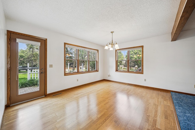 741 3rd St NE, Faribault, MN 55021 - unfurnished room featuring plenty of natural light, a chandelier, a textured ceiling, light wood-style flooring, and beam ceiling