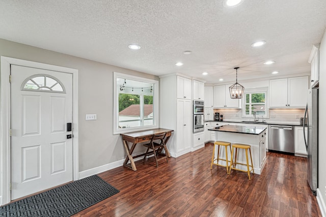 18160 Echo Ave, Faribault, MN 55021 - kitchen with appliances with stainless steel finishes, dark wood-style flooring, a center island, decorative backsplash, and white cabinetry