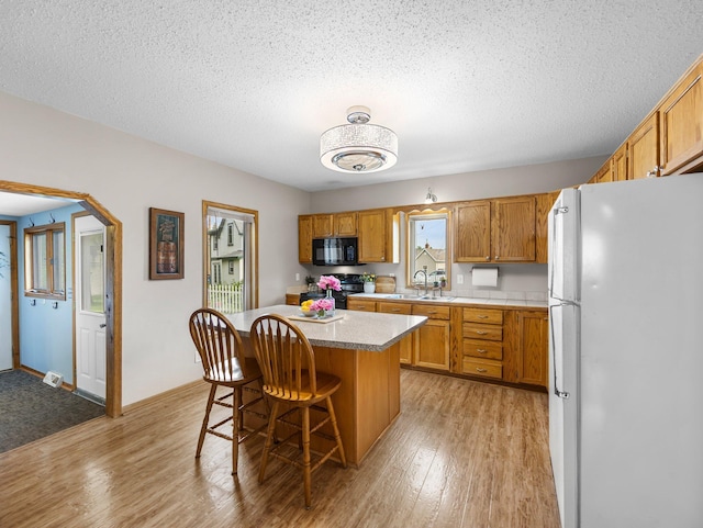 45 Oak Ave S, Maple Lake, MN 55358 - kitchen with black appliances, a kitchen island, brown cabinets, light wood-type flooring, and light countertops