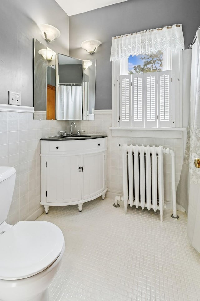 228 Sidney St W, Saint Paul, MN 55107 - bathroom with radiator heating unit, tile walls, tile patterned flooring, vanity, and a wainscoted wall