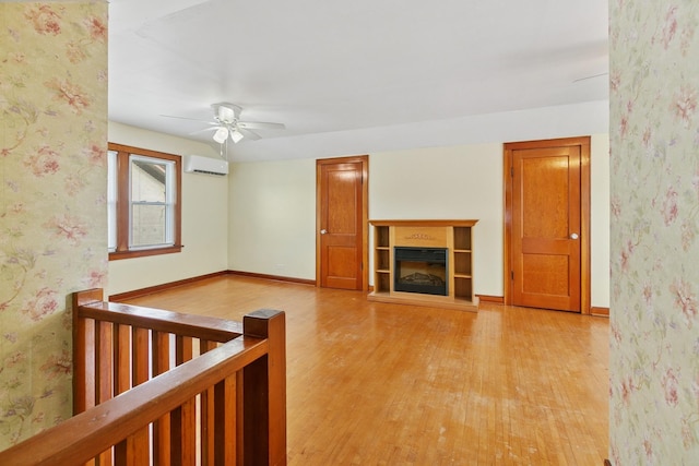 228 Sidney St W, Saint Paul, MN 55107 - unfurnished living room with a wall unit AC, light wood-style flooring, a ceiling fan, a glass covered fireplace, and wallpapered walls