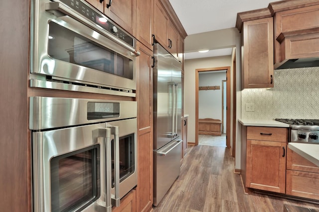 6033 Sargent Ct N, Lino Lakes, MN 55110 - kitchen featuring appliances with stainless steel finishes, wood finished floors, tasteful backsplash, brown cabinets, and light countertops