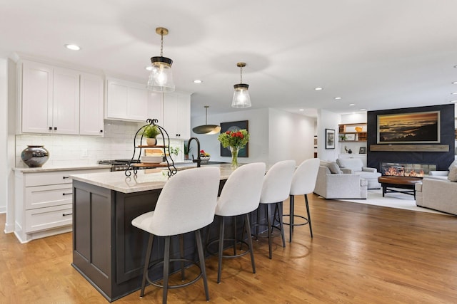 3930 Cottage Ln, Minnetonka, MN 55305 - kitchen featuring white cabinets, a kitchen island with sink, light wood-type flooring, a breakfast bar, and decorative backsplash