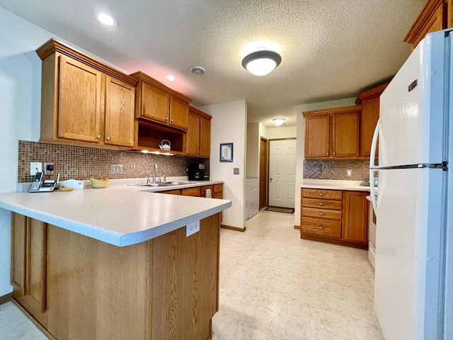 727 Cloud St NW, Bemidji, MN 56601 - kitchen with freestanding refrigerator, a sink, a peninsula, brown cabinetry, and backsplash
