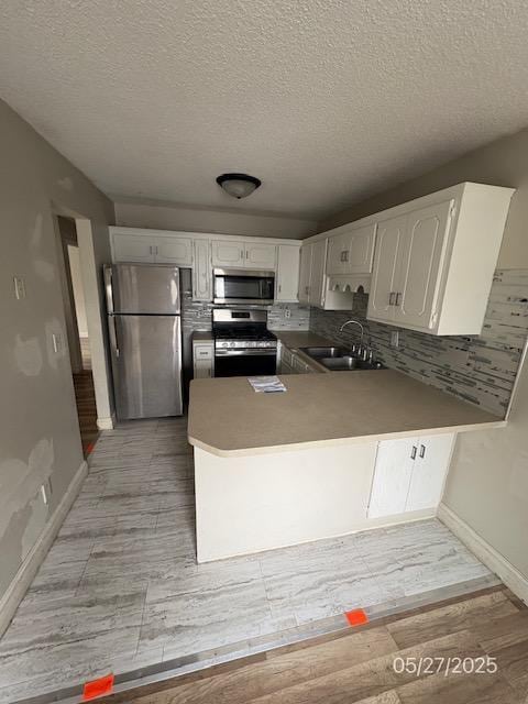 6769 Humboldt Ave N, Brooklyn Center, MN 55430 - kitchen with appliances with stainless steel finishes, a sink, white cabinets, a peninsula, and baseboards