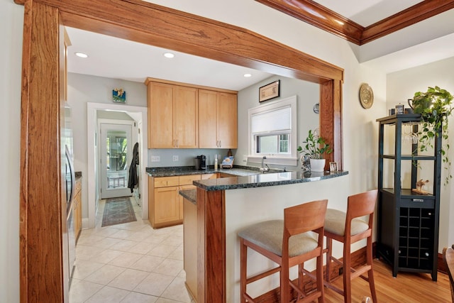 3229 Fremont Ave S, Minneapolis, MN 55408 - kitchen with ornamental molding, a breakfast bar, light brown cabinets, a peninsula, and dark stone counters