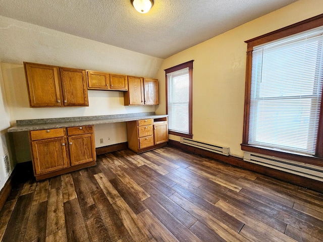 324 Holcombe Ave, Litchfield, MN 55355 - kitchen featuring built in study area, vaulted ceiling, brown cabinets, dark wood-style floors, and a textured ceiling