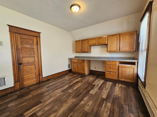 324 Holcombe Ave, Litchfield, MN 55355 - kitchen featuring built in study area, dark wood-style floors, lofted ceiling, brown cabinets, and a textured ceiling