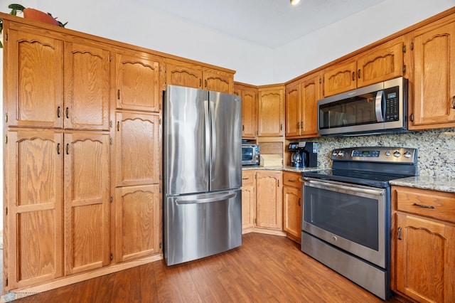 3306 26th Ave S, Fargo, ND 58103 - kitchen with appliances with stainless steel finishes, dark wood-style flooring, tasteful backsplash, brown cabinetry, and light stone counters