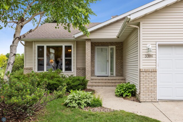 3306 26th Ave S, Fargo, ND 58103 - view of exterior entry featuring brick siding, an attached garage, and a shingled roof