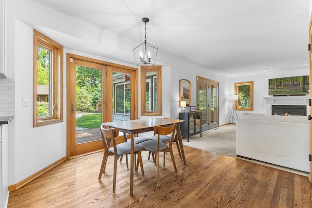 13870 Daphne Ln, Rosemount, MN 55068 - dining room with a lit fireplace, baseboards, a chandelier, and light wood-style floors