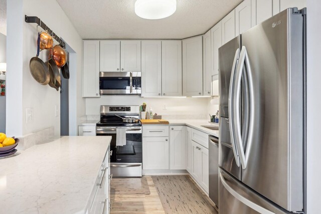 78 10th St E Unit 3009, Saint Paul, MN 55101 - kitchen featuring stainless steel appliances, light wood-style floors, white cabinetry, a textured ceiling, and light stone countertops