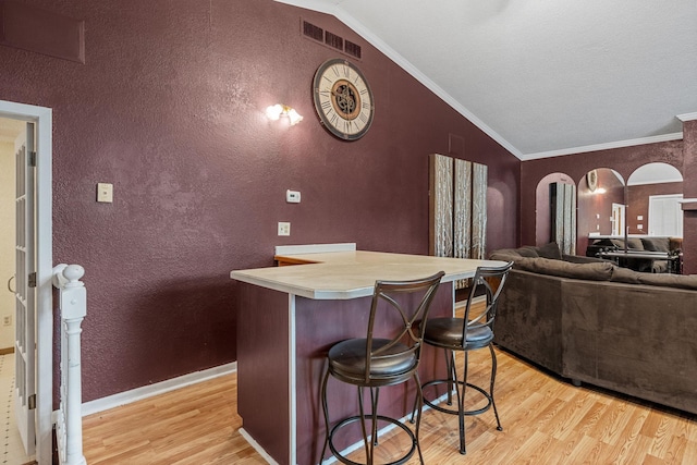 2101 6th Ave NE, Austin, MN 55912 - kitchen with vaulted ceiling, light wood-style flooring, a textured wall, arched walkways, and a breakfast bar