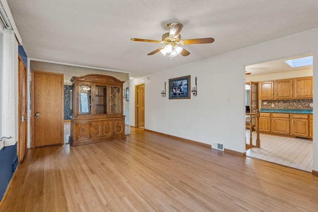 2101 6th Ave NE, Austin, MN 55912 - unfurnished living room featuring light wood-style flooring, a textured ceiling, ceiling fan, a skylight, and baseboards
