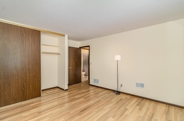7880 Rimbley Rd, Woodbury, MN 55125 - unfurnished bedroom featuring light wood finished floors, a closet, a textured ceiling, and ensuite bathroom