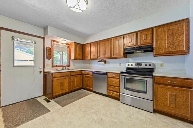 635 5th St, Windom, MN 56101 - kitchen with stainless steel appliances, under cabinet range hood, brown cabinetry, light countertops, and a textured ceiling