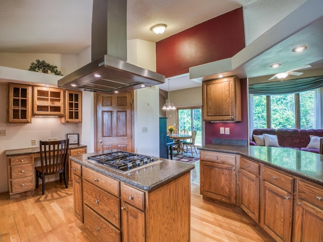 22152 Polaris Rd NW, Puposky, MN 56667 - kitchen featuring island exhaust hood, stainless steel gas stovetop, light wood-type flooring, brown cabinetry, and glass insert cabinets