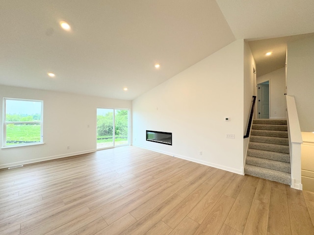 7031 Lannon Ave NE, Otsego, MN 55301 - unfurnished living room with light wood-style floors, recessed lighting, stairs, a glass covered fireplace, and vaulted ceiling