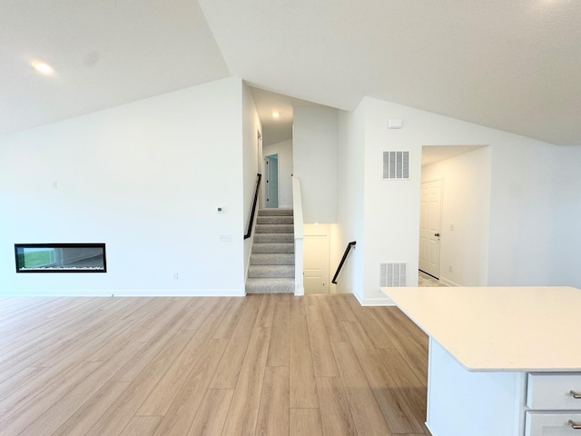 7031 Lannon Ave NE, Otsego, MN 55301 - unfurnished living room with lofted ceiling, light wood-style floors, and a glass covered fireplace