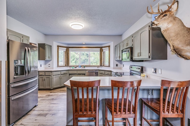 3220 Vine St, Cambridge, MN 55008 - kitchen featuring stainless steel appliances, a peninsula, gray cabinetry, a textured ceiling, and light wood-style flooring