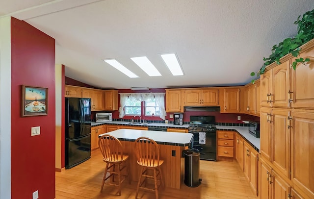 10196 48th St, Clear Lake, MN 55319 - kitchen with black appliances, under cabinet range hood, light wood-style flooring, vaulted ceiling, and a breakfast bar