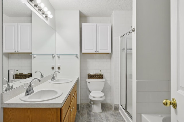 2936 18th Ave E, Shakopee, MN 55379 - bathroom featuring a textured ceiling, double vanity, tile walls, wood finished floors, and a shower stall