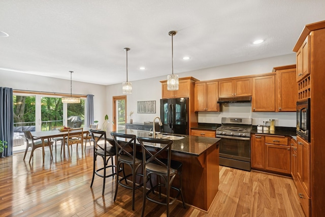 1020 Bliss Ln, Bloomington, MN 55431 - kitchen featuring black appliances, under cabinet range hood, light wood finished floors, brown cabinetry, and a kitchen bar