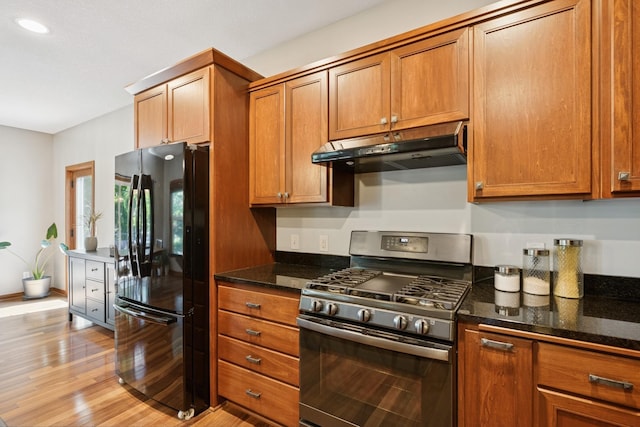1020 Bliss Ln, Bloomington, MN 55431 - kitchen with freestanding refrigerator, stainless steel gas stove, under cabinet range hood, dark stone countertops, and brown cabinets