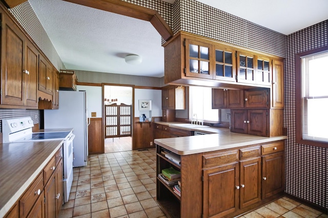 930 Minekahda Pl, Owatonna, MN 55060 - kitchen featuring white range with electric cooktop, wallpapered walls, a peninsula, glass insert cabinets, and brown cabinetry