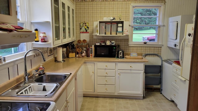 112 240th St N, Eglon Twp, MN 56549 - kitchen with stacked washer and clothes dryer, black microwave, healthy amount of natural light, and white cabinets