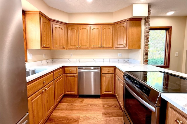 3140 Fremont Ave S, Minneapolis, MN 55408 - kitchen with appliances with stainless steel finishes, light wood-type flooring, brown cabinetry, a textured ceiling, and light stone countertops