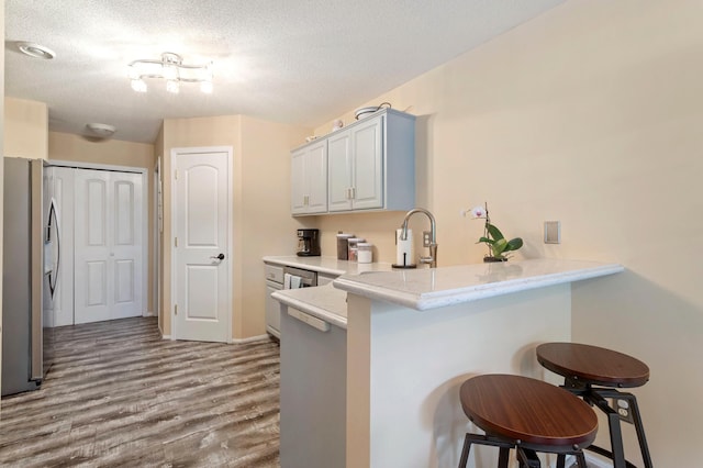 8475 121st Ave N, Champlin, MN 55316 - kitchen with stainless steel fridge, a peninsula, a breakfast bar, wood finished floors, and a textured ceiling